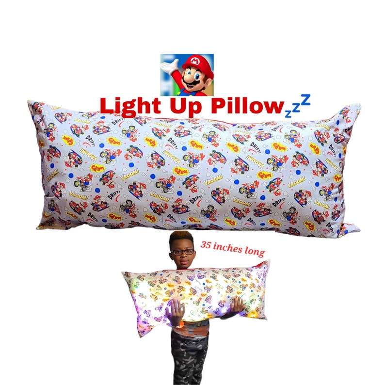 May include: A light-up pillow featuring a Mario Kart design with the words "Vroom!" and "Drift!" printed on it. The pillow is 35 inches long and is shown being held by a child.