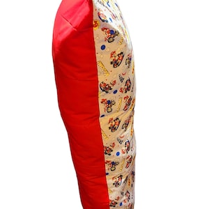 May include: A red and white pillow with a cartoon character print. The pillow has a red side and a white side with a cartoon character print. The print features a cartoon character driving a race car. The print also includes the words "Wooom!" and "Prrrrm!"