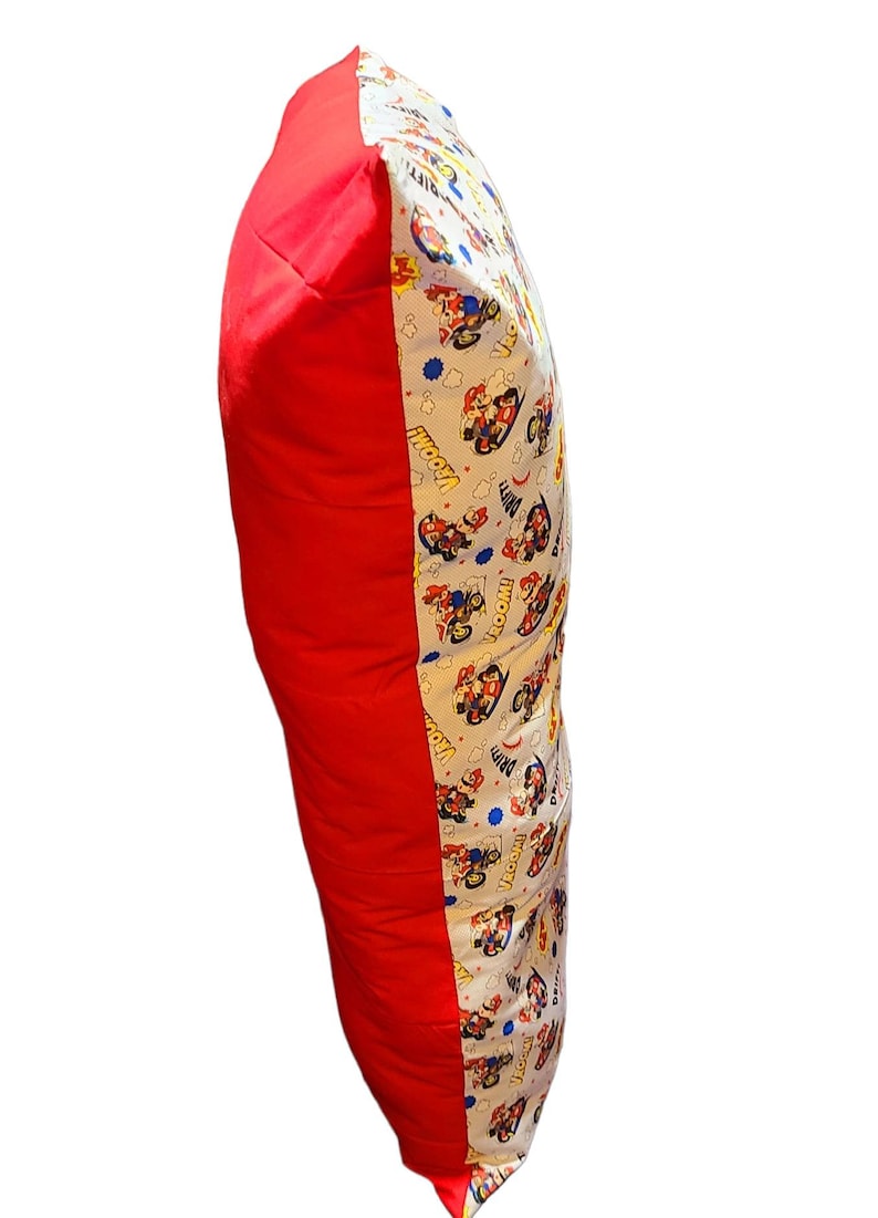 May include: A red and white pillow with a cartoon character print. The pillow has a red side and a white side with a cartoon character print. The print features a cartoon character driving a race car. The print also includes the words "Wooom!" and "Prrrrm!"