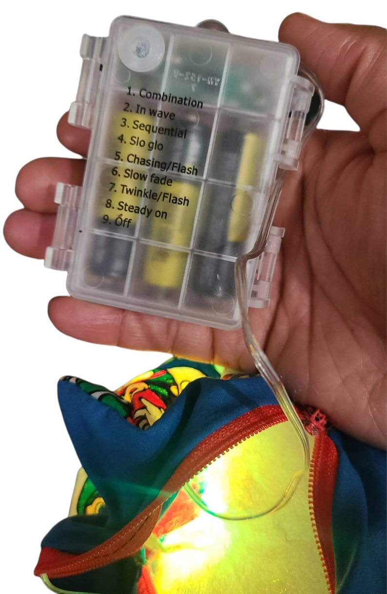 May include: A clear plastic battery pack with a list of light modes: Combination, In wave, Sequential, Slo glo, Chasing/Flash, Slow fade, Twinkle/Flash, Steady on, Off. The battery pack is connected to a blue and red fabric with a yellow light shining through.