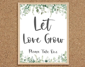 May include: A white sign with a wooden frame and a green eucalyptus leaf border. The sign says "Let Love Grow" and "Please Take One".
