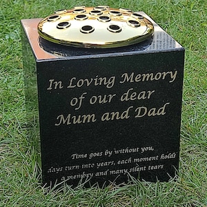 May include: Black granite memorial with a gold flower vase on top. The inscription reads "In Loving Memory of our dear Mum and Dad. Time goes by without you, days turn into years, each moment holds a memory and many silent tears."