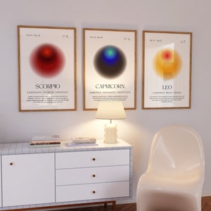 Puede incluir: Tres impresiones enmarcadas con los signos del zod&iacute;aco Escorpio, Capricornio y Leo. Cada impresi&oacute;n presenta un c&iacute;rculo degradado con un s&iacute;mbolo y el nombre del signo. Las impresiones est&aacute;n colgadas en una pared blanca con una l&aacute;mpara blanca y una silla blanca en primer plano.