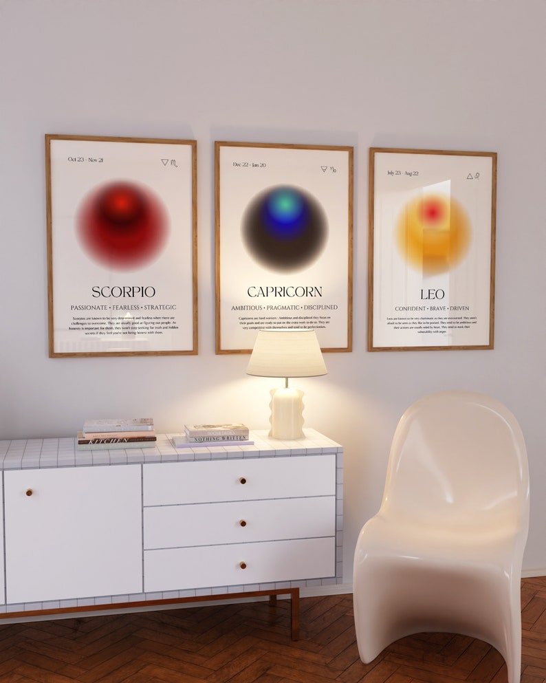 Puede incluir: Tres impresiones enmarcadas con los signos del zod&iacute;aco Escorpio, Capricornio y Leo. Cada impresi&oacute;n presenta un c&iacute;rculo degradado con un s&iacute;mbolo y el nombre del signo. Las impresiones est&aacute;n colgadas en una pared blanca con una l&aacute;mpara blanca y una silla blanca en primer plano.