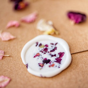 Peut inclure: Un sceau de cire blanc avec des p&eacute;tales de rose s&eacute;ch&eacute;s incrust&eacute;s dans la cire. Le sceau est sur une surface brune avec d'autres p&eacute;tales de rose &eacute;parpill&eacute;s autour.