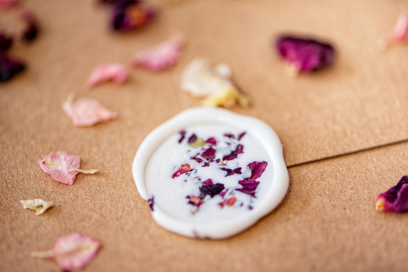 Peut inclure: Un sceau de cire blanc avec des p&eacute;tales de rose s&eacute;ch&eacute;s incrust&eacute;s dans la cire. Le sceau est sur une surface brune avec d'autres p&eacute;tales de rose &eacute;parpill&eacute;s autour.