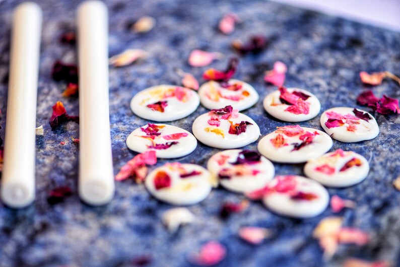 Peut inclure: Des disques de chocolat blanc avec des p&eacute;tales de rose s&eacute;ch&eacute;s sur une surface bleue.