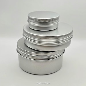 May include: Three round silver metal tins stacked vertically in descending order of size. Each container features a smooth, cylindrical body and a matching screw-top lid with a textured, ribbed edge for grip. The text @missarohma is visible.