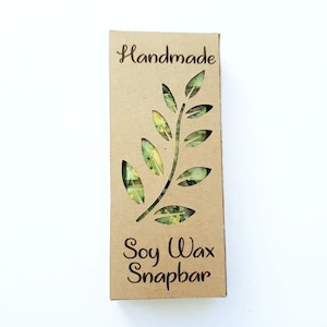 Op de afbeelding: Een bruine kartonnen doos met een uitgesneden ontwerp van een groene, bladerrijke tak. De doos heeft de tekst "Handmade" bovenaan en "Soy Wax Snapbar" onderaan.