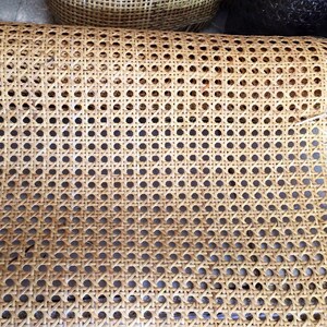 May include: A close-up of a woven cane webbing material, often used for chair seats and backs. The material is light brown and has a grid pattern with round holes.