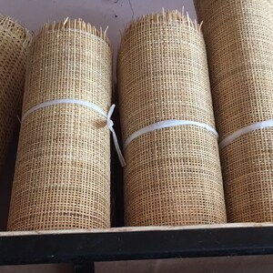 Pu&ograve; includere: Quattro rotoli di materiale tessuto naturale, forse per l'artigianato o la tessitura, sono impilati su uno scaffale nero. Ogni rotolo &egrave; legato con un nastro bianco.