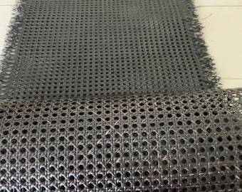 Può includere: Tessuto di vimini nero intrecciato, un materiale utilizzato per sedili e schienali di sedie. Il vimini è arrotolato e mostra il complesso motivo di intreccio.