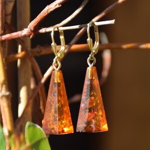 May include: A pair of gold tone dangle earrings with amber teardrop shaped stones. The stones are a deep orange color and have a faceted design.