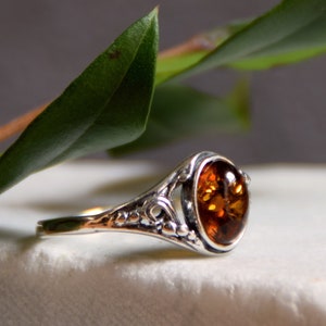 Op de afbeelding: Een zilveren ring met een ovale amberkleurige edelsteen. De ring heeft een delicaat, versierd ontwerp.