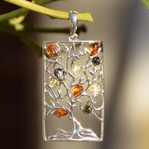 Pode incluir: Pingente retangular de prata com um design de árvore com pedras âmbar. O pingente tem uma argola para uma corrente e está suspenso por um caule verde. As pedras âmbar variam em cor, do amarelo claro ao castanho escuro.