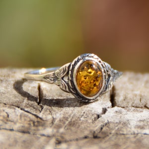 Op de afbeelding: Een zilveren ring met een ovale amberkleurige edelsteen, gezet in een gedetailleerd filigraanontwerp.