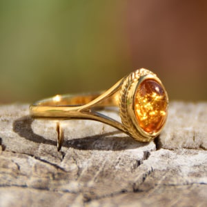 Peut inclure: Une bague en or avec une grande pierre précieuse en ambre. La bague a un design délicat à bande fendue.