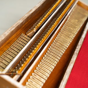 May include: Close-up of a wooden box containing numerous small, rectangular, brass-coloured pieces. The box has a natural wood finish and a red fabric lining. The image is well-lit, highlighting the details.