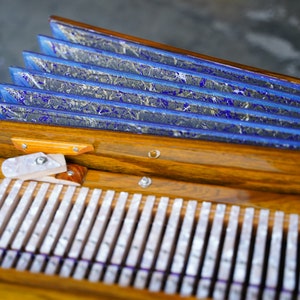May include: Detailed view of an accordion, featuring a wooden body and blue and grey bellows. The white keys and intricate design suggest a handcrafted instrument. A musical instrument.