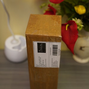 K&ouml;nnte beinhalten: Ein brauner Karton mit einem wei&szlig;en Etikett, auf dem "Happily Ever After" und "Courier Delivery Note" steht. Der Karton steht auf einer dunklen Holzoberfl&auml;che.