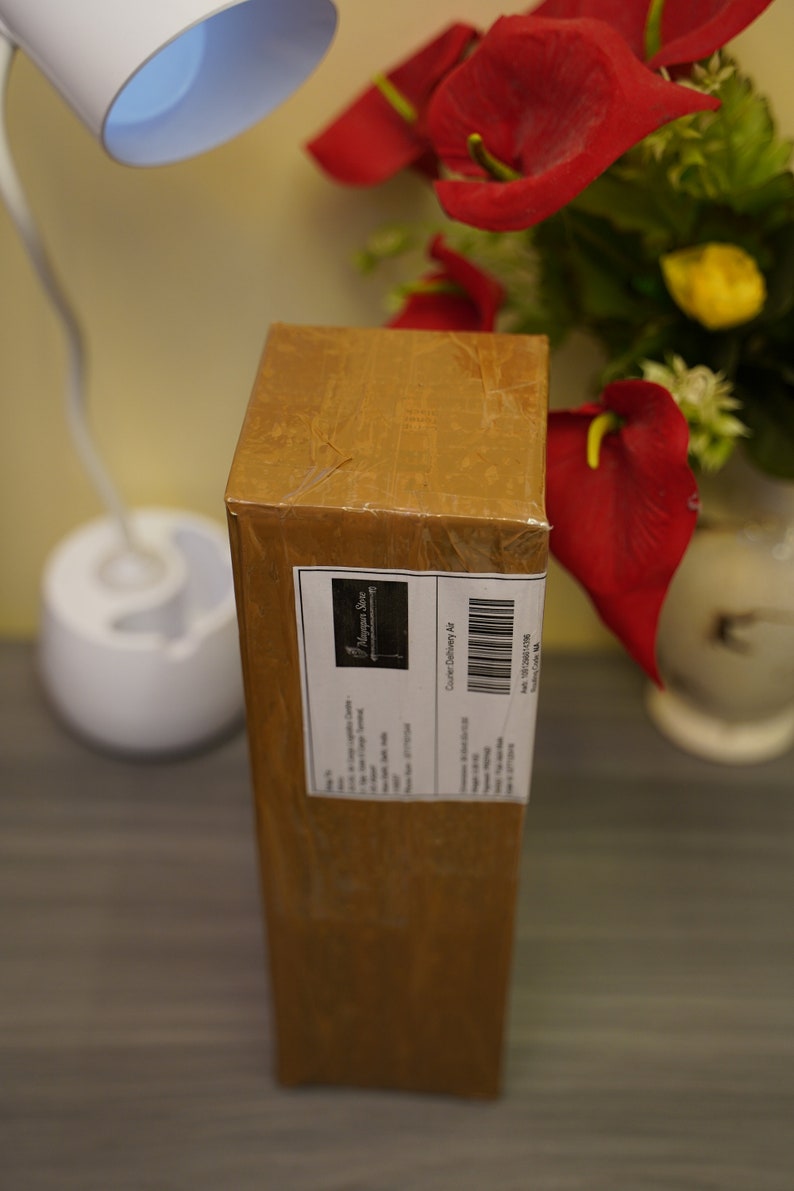 K&ouml;nnte beinhalten: Ein brauner Karton mit einem wei&szlig;en Etikett, auf dem "Happily Ever After" und "Courier Delivery Note" steht. Der Karton steht auf einer dunklen Holzoberfl&auml;che.