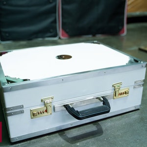 May include: A white, rectangular, hard-sided case with a silver trim and a black handle. The case has two locks with combination dials and a white interior.