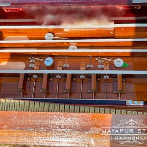 Pode incluir: Um harm&oacute;nio de madeira com acabamento castanho e interior branco. O harm&oacute;nio tem uma fila de teclas e um fole. O harm&oacute;nio est&aacute; aberto e o fole &eacute; vis&iacute;vel. O harm&oacute;nio est&aacute; etiquetado como "MAYAPUR STORE HARMONIUM".