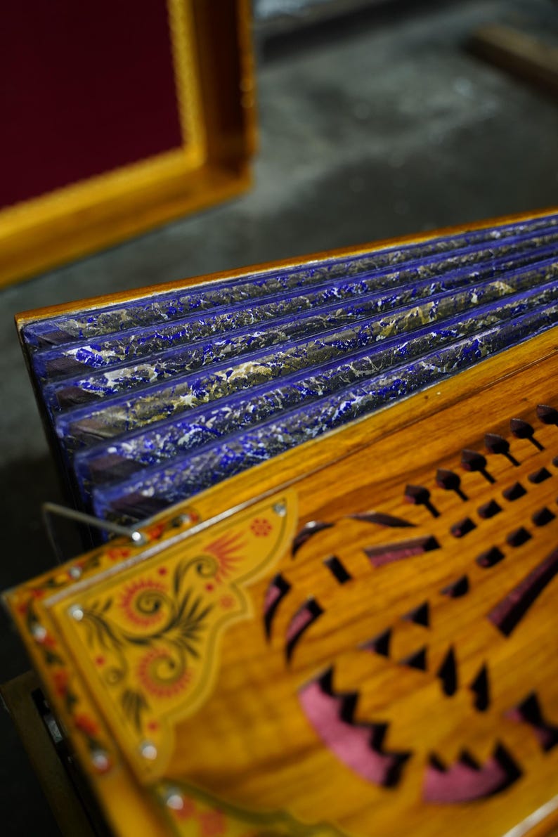 K&ouml;nnte beinhalten: Ein Holzmusikinstrument mit einem blau und gold lackierten Blasebalg und aufwendigen Schnitzereien. Das Instrument hat eine Reihe von L&ouml;chern auf der Vorderseite und ein dekoratives Blumenmuster.