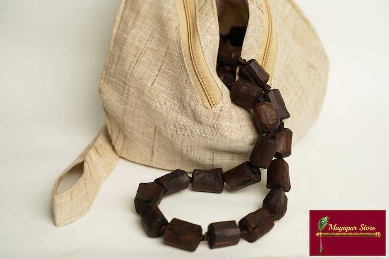 K&ouml;nnte beinhalten: Eine beigefarbene Leinentasche mit Rei&szlig;verschluss und einer braunen Holzperlenkette. Die Tasche hat einen Henkel und ist aus einem Naturstoff gefertigt.