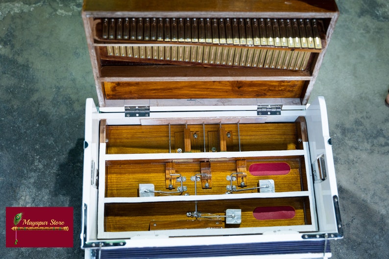 May include: An open wooden case with a white interior. The case has a row of metal reeds and a series of wooden levers and pedals. The case is open and the interior is visible. The case is made of wood and has a natural finish.