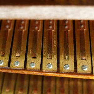K&ouml;nnte beinhalten: Nahaufnahme einer Reihe von messingfarbenen Klaviertasten mit einem Holzrahmen. Die Tasten sind mit dem Text "FR. STEINMAYER & CO." beschriftet.