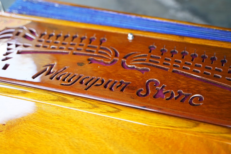 May include: Close-up of a wooden decorative piece with the text "Mayapur Store" carved into it. The wood has a warm, reddish-brown hue, with a glossy finish. The text is in a stylized font.