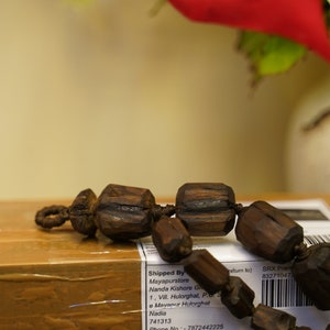 K&ouml;nnte beinhalten: Eine braune Holz-Mala-Kette mit dunkelbraunen Perlen und einer Schnur aus dunkelbraunem Garn. Die Kette liegt auf einem braunen Karton mit einem wei&szlig;en Etikett, auf dem steht "Shipped By Mayapurstore Nanda Kishore Gh 1, Vill. Hulorghat, P.S. S e Mayanur Hulorghat Nadia 741313 Phone No.: 7872442225 Alternate No.: - 9679103955 return to) SRX Prem 832710472 Product Description: Puja Japa Mala SKU: MSJM002 | QTY.: 1 Total: Rs.6642.42 Buyer Name: Trevor Krenzelak Invoice No. Retail00014 | Invoice Date :2024-05-02 GSTIN:19BEDPG7899M1ZK"