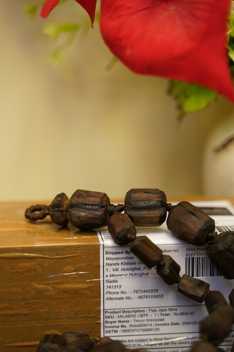 K&ouml;nnte beinhalten: Eine braune Holz-Mala-Kette mit dunkelbraunen Perlen und einer Schnur aus dunkelbraunem Garn. Die Kette liegt auf einem braunen Karton mit einem wei&szlig;en Etikett, auf dem steht "Shipped By Mayapurstore Nanda Kishore Gh 1, Vill. Hulorghat, P.S. S e Mayanur Hulorghat Nadia 741313 Phone No.: 7872442225 Alternate No.: - 9679103955 return to) SRX Prem 832710472 Product Description: Puja Japa Mala SKU: MSJM002 | QTY.: 1 Total: Rs.6642.42 Buyer Name: Trevor Krenzelak Invoice No. Retail00014 | Invoice Date :2024-05-02 GSTIN:19BEDPG7899M1ZK"