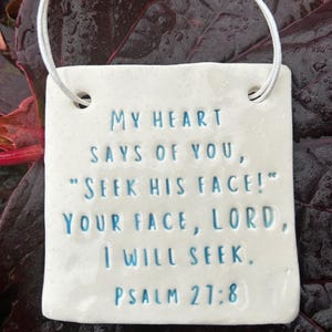 Könnte beinhalten: Ein weißes Keramikquadrat mit dem Text "MY HEART SAYS OF YOU, 'SEEK HIS FACE!' YOUR FACE, LORD, I WILL SEEK. PSALM 27:8" in blauen Buchstaben. Eine weiße Schnur ist zum Aufhängen befestigt.