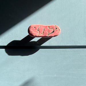 May include: Two pink ceramic cabinet pulls with a textured surface are mounted on a light blue cabinet. The pulls are rectangular with rounded edges and a crackled design. The cabinet is divided by a horizontal line.