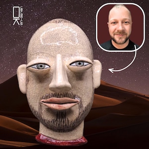 May include: A ceramic sculpture of a human head with a crackled beige glaze, almond-shaped eyes, a prominent nose, and painted facial hair. The base is a dark red band. A small inset photo shows a person with a similar appearance and a beard.
