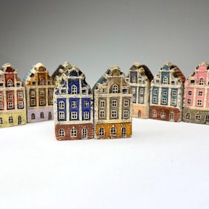 Puede incluir: Una fila de casas en miniatura pintadas en varios colores, incluyendo azul, verde, amarillo, rosa y marrón. Cada casa tiene un diseño único y presenta pequeñas ventanas y puertas.