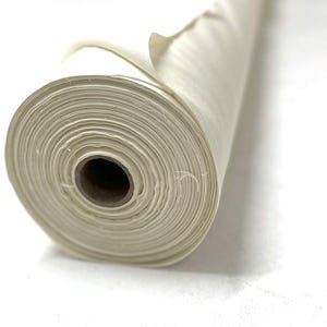 May include: A rolled-up length of off-white fabric, showing tightly packed layers. The material looks like a natural fibre, perhaps cotton or linen, and is unprinted. The central core is a dark brown cardboard tube.