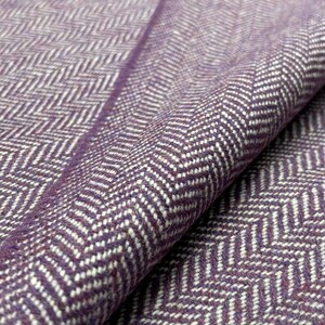 May include: Close-up of a purple and white herringbone fabric. The fabric is folded, showing the texture and pattern. The weave is tight, with a mix of purple and white threads creating the chevron design.