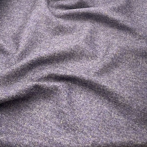 May include: Close-up of a textured fabric in shades of purple. The material has a woven appearance with subtle variations in color and texture, creating a soft, inviting look. The fabric is draped, showing folds and shadows.