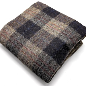 May include: Folded pocket square in a traditional plaid design. The fabric displays a blend of brown, navy, and red hues. The pocket square is crafted from a textured material, possibly wool or a wool mix, and is neatly folded.