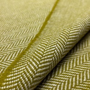 May include: Close-up of a folded fabric with a herringbone pattern. The fabric is a blend of olive green and white, with the pattern creating a textured appearance. The weave is visible, and the fabric appears soft and pliable.