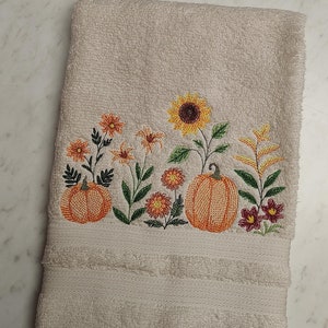 May include: White hand towel with embroidered pumpkins, sunflowers, and fall flowers in shades of orange, yellow, and red.