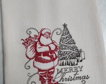 May include: Embroidered kitchen towel with a red and black design of Santa Claus carrying a bag of gifts and a Christmas tree. The text "Merry Christmas" is embroidered in black below the design.
