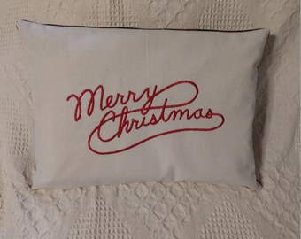 May include: White pillow with red embroidered cursive text that reads "Merry Christmas".