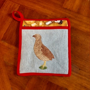 May include: Red and blue pot holder with a brown and white embroidered quail on a light blue background.