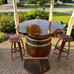 May include: A wooden table with a live edge epoxy resin top and three matching wooden stools. The table is made from a repurposed wine barrel and the stools are also made from wine barrels.