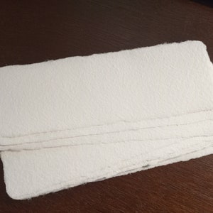 May include: A stack of white, textured paper sheets with deckled edges.