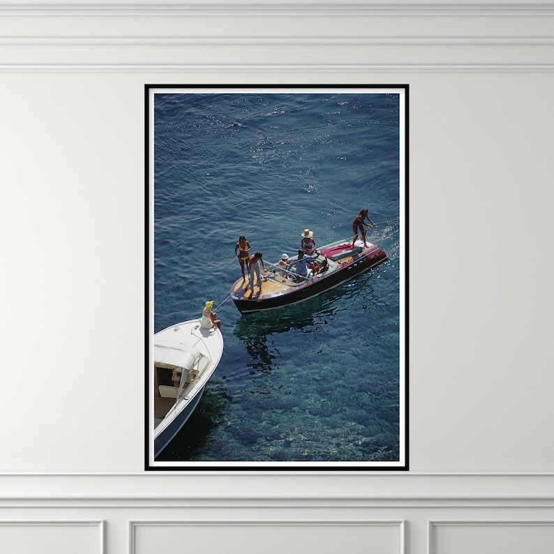 Peut inclure: Une impression encadr&eacute;e repr&eacute;sentant deux bateaux sur l'eau. L'un est blanc, l'autre est un bateau en bois avec des personnes &agrave; bord. L'eau est d'un bleu profond et l'image est encadr&eacute;e en noir.